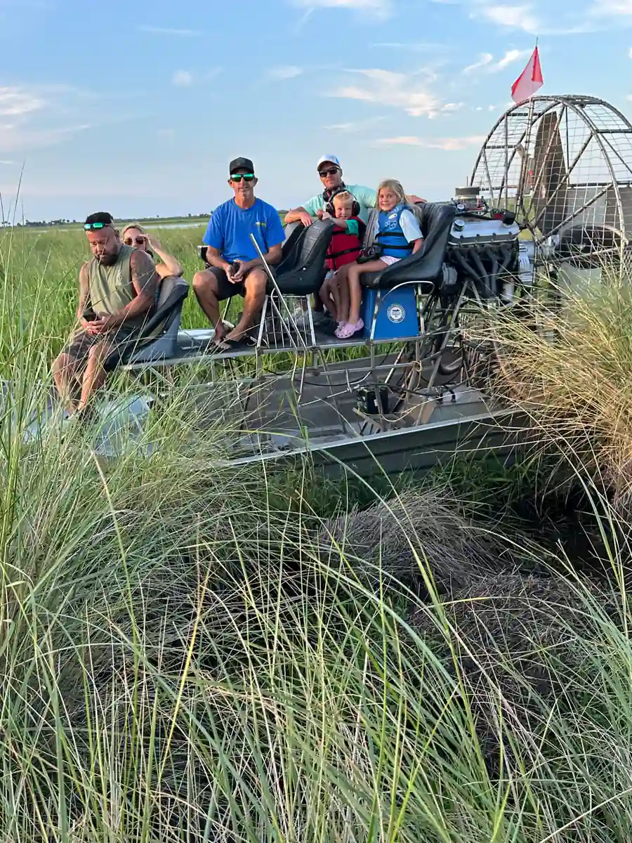 Six guests including two young girls in life vests seated on an airboat nosed into tall marsh grass beside an alligator nest