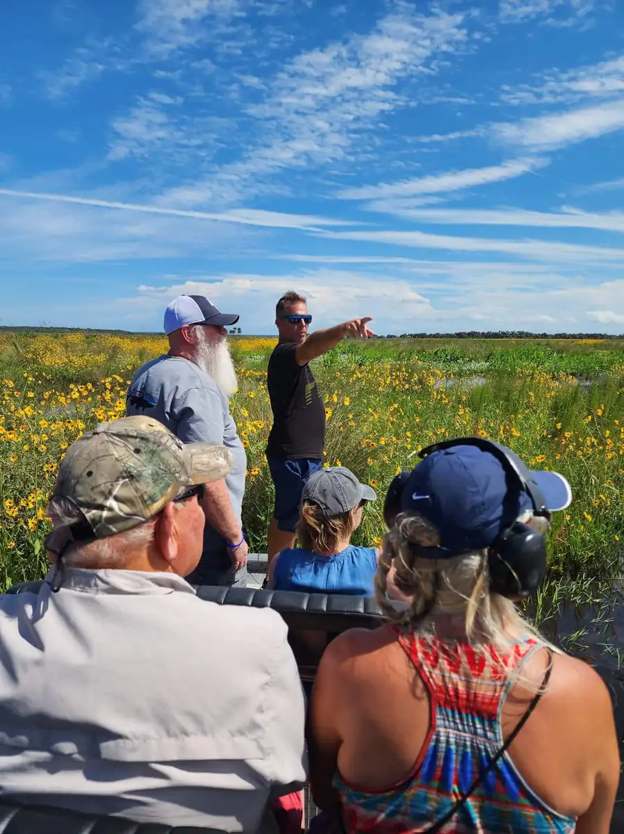 Captain Seth pointing across acres of yellow brown eyed susans while guests in headsets watch from the airboat