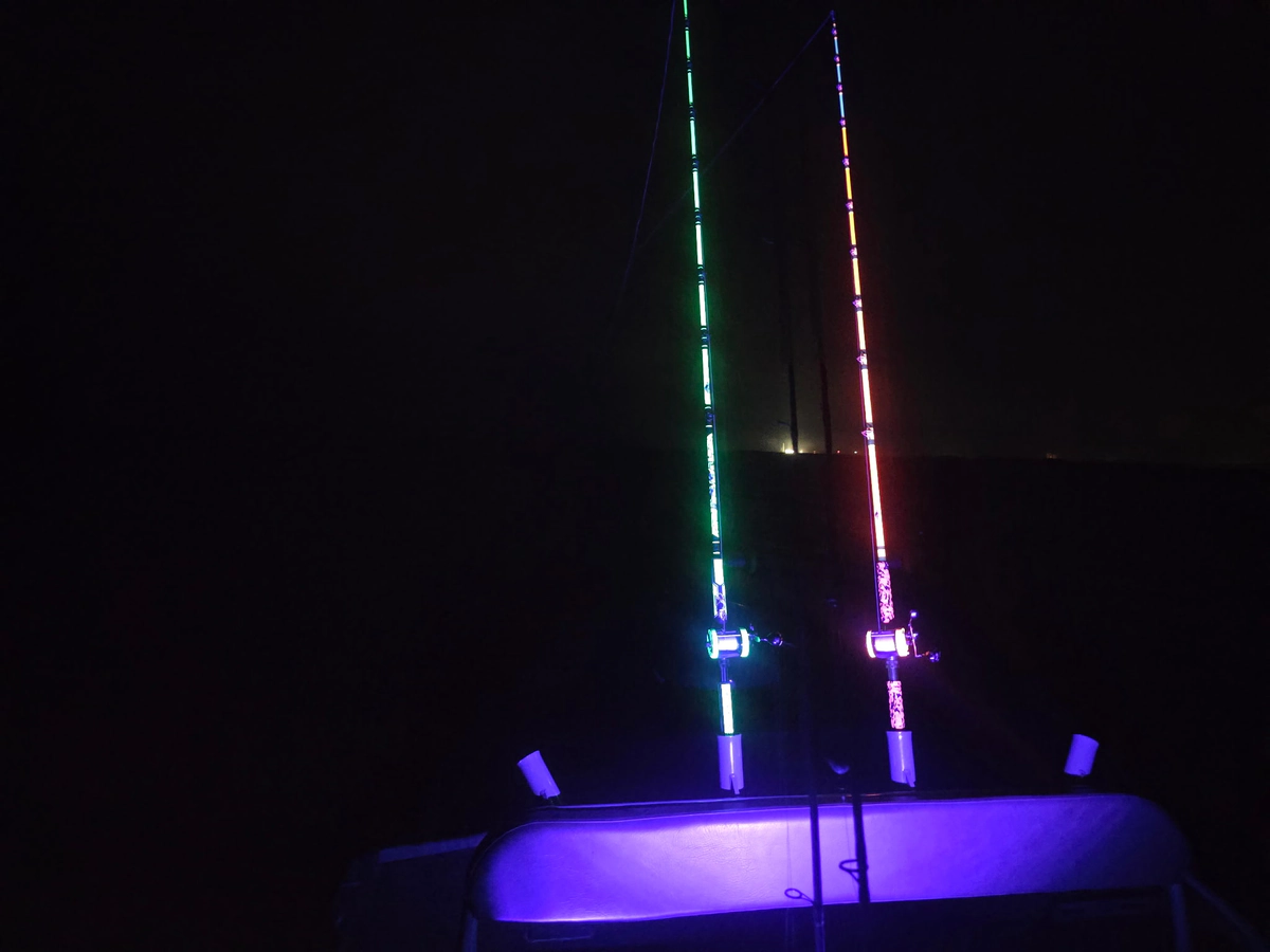 Two fishing rods glowing bright green and bright red against a black night sky over the water