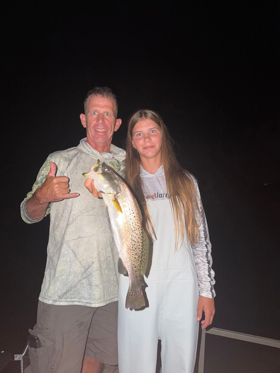 A father and his daughter holding up a spotted seatrout together on the boat at night