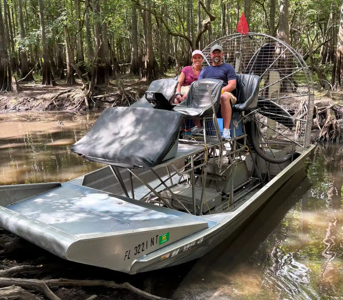 A couple seated in the elevated seats of an airboat sitting in a shaded cypress slough on the St. Johns River