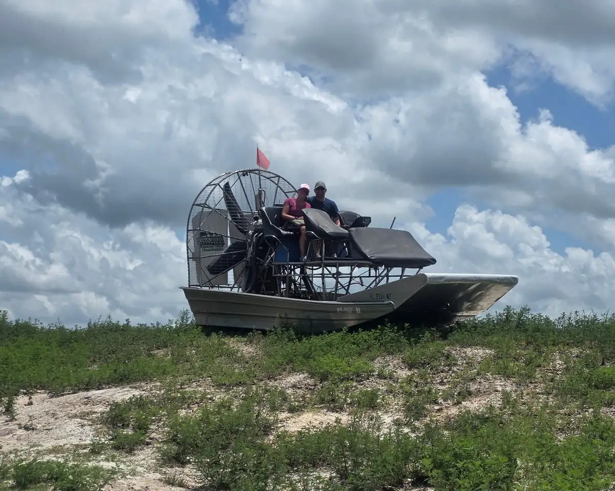 An airboat sitting up on a dry sand rise well away from the water under towering summer clouds