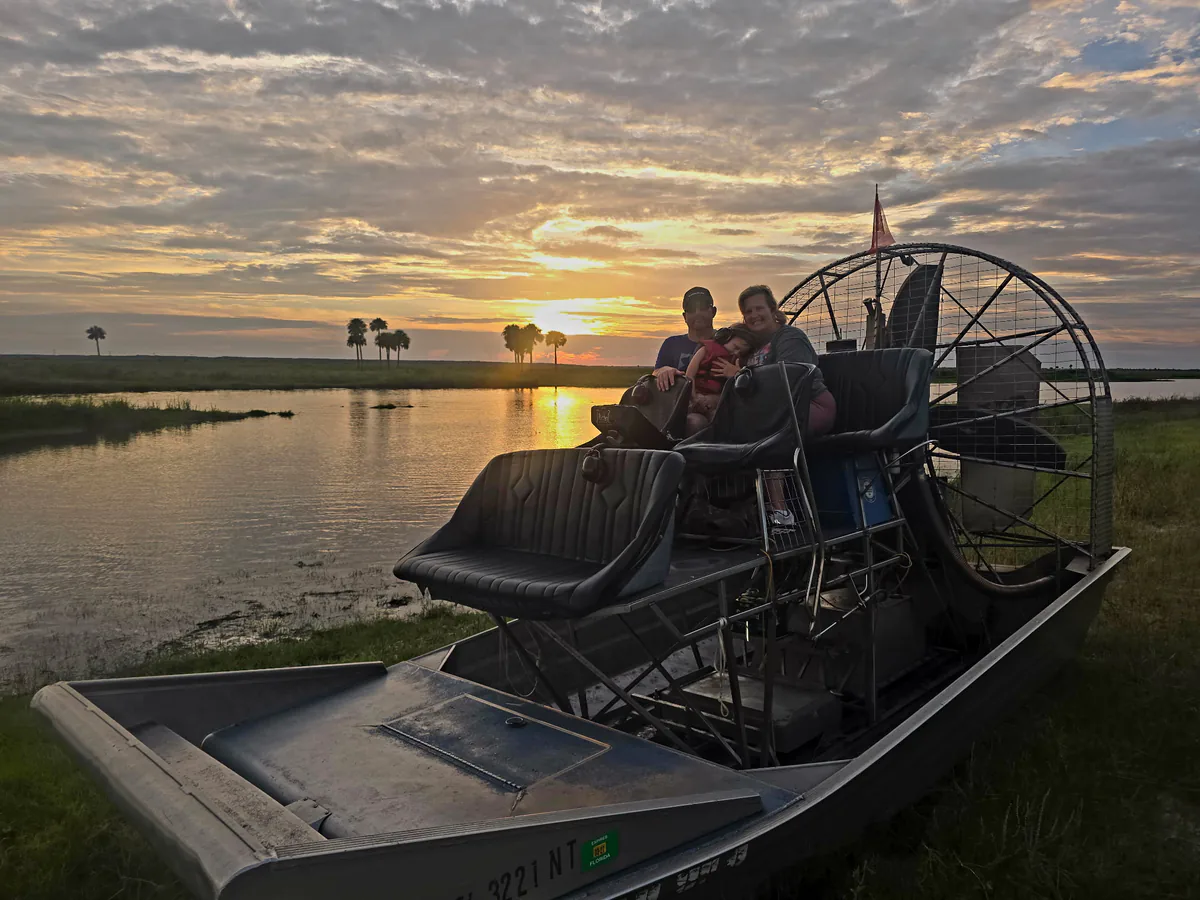 Guests seated high in the lifted airboat seats watching the sun drop behind palms across the water
