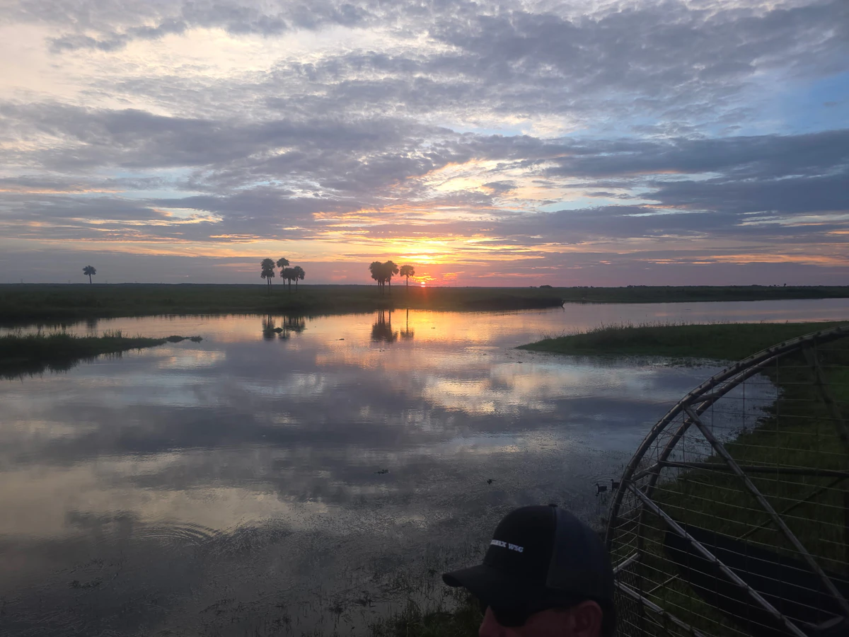 A couple seated in the lifted seats of an airboat parked on the bank as the sun sets over the flooded prairie